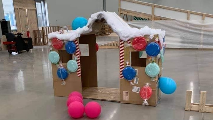 A cardboard house decorated by coloured plates, in front of a series of coloured foam mats.