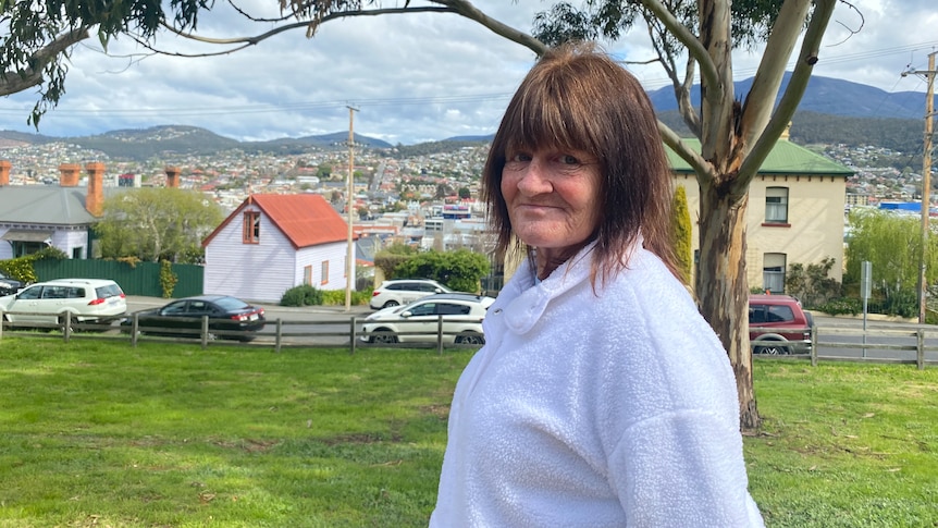 A woman wearing a jumper smiles at the camera, with Hobart visible in the background.