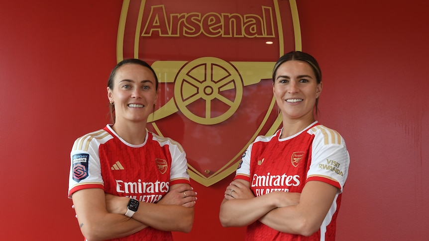 Two players in red jerseys pose for a photo in front of an emblem.