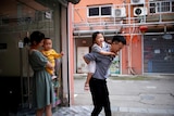 A man and a woman each carry a child as they leave a building. 