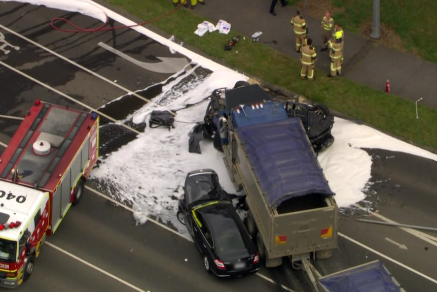 An aerial shot of two cars hit by a truck, one completely crushed, and emergency services walking on scene.