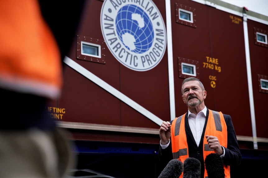 A man wearing a high visibility vest standing in front of an Australian Antarctic Program sign