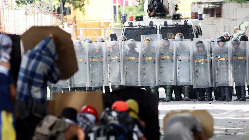 Police stand behind shields in the background as protestors hide behind home made shields.