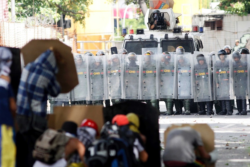 Police stand behind shields in the background as protestors hide behind home made shields.