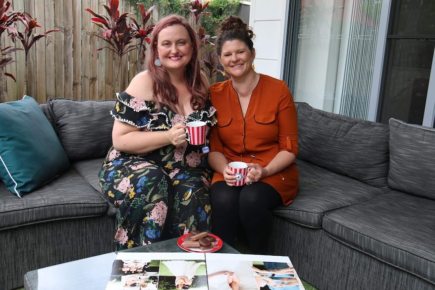 Kate Mackie and wife Leonie Clark look through their wedding album on a couch in their patio.