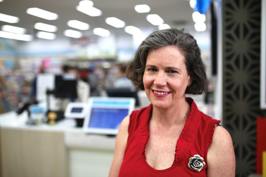A woman in a red dress smiles in front of a newsagent.