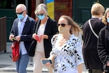 People of different ages are seen walking in a street, all wearing face masks.