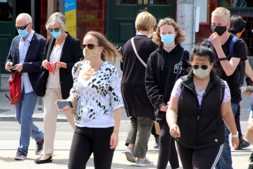 People of different ages are seen walking in a street, all wearing face masks.