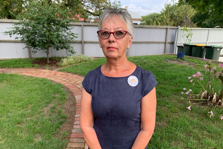 a woman with cropped grey hair stares at the camera. She's not smiling.