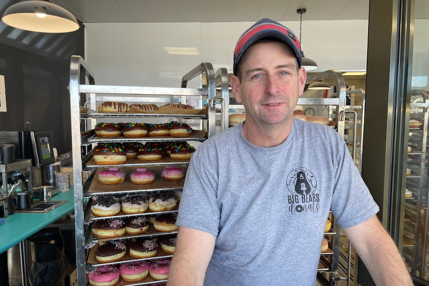 A man standing in a shop in front of donuts he made