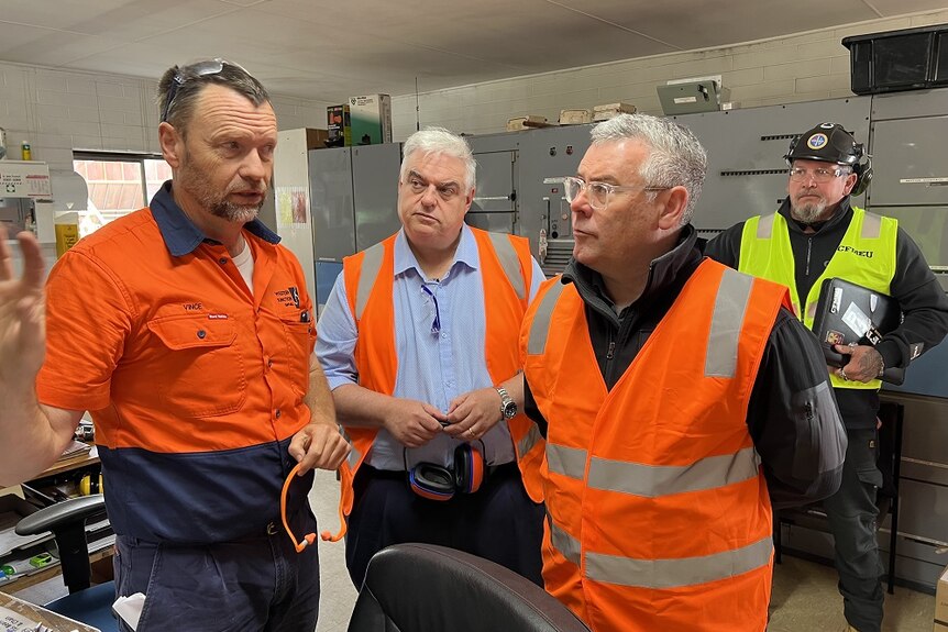 Two men in high vis jackets talk at a timber mill near Launceston