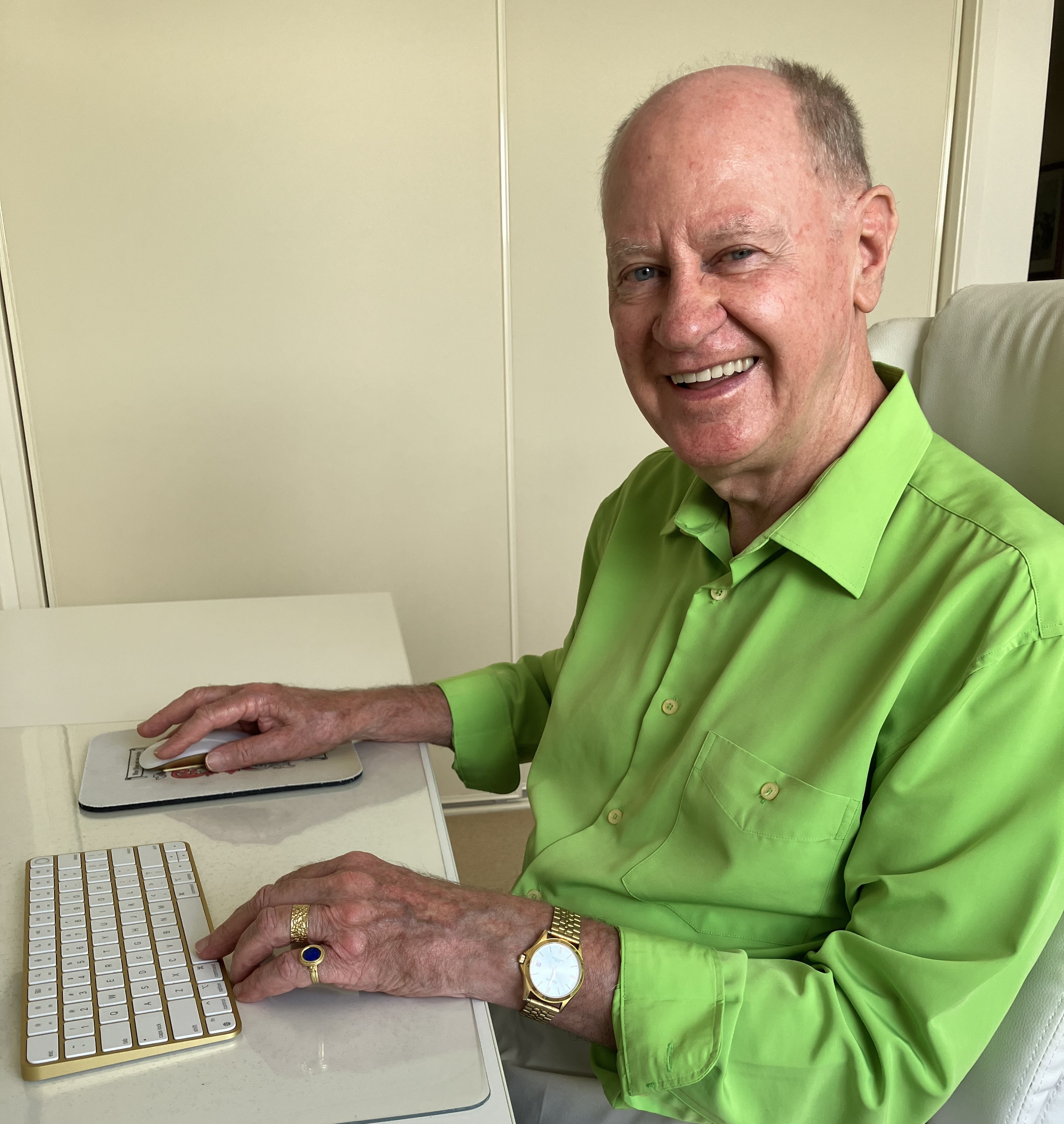 Un hombre con una camisa abotonada sonríe mientras está sentado en una silla de escritorio. 