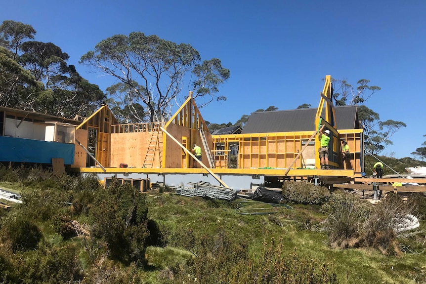 A team of builders in high vis working on a building site in a remote bush setting in sunny weather