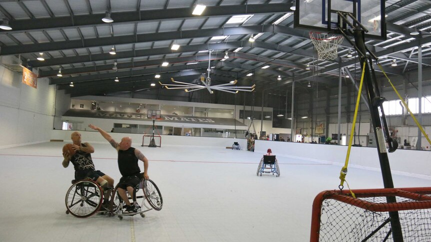 Two men in wheelchairs playing basketball in a large stadium.