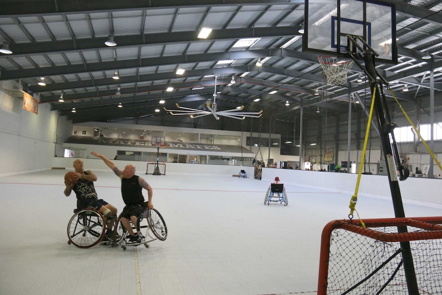 Two men in wheelchairs playing basketball in a large stadium.