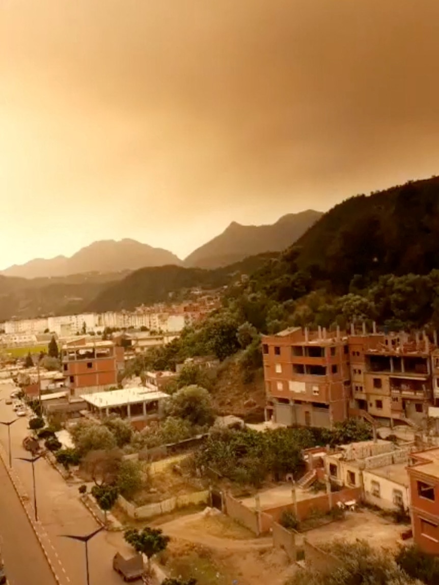 Smoke rises over a town, turning the sky a brownish orange.