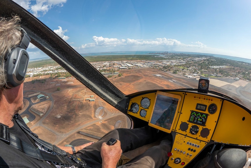 A man with grey hair and a headset on steers the controls in