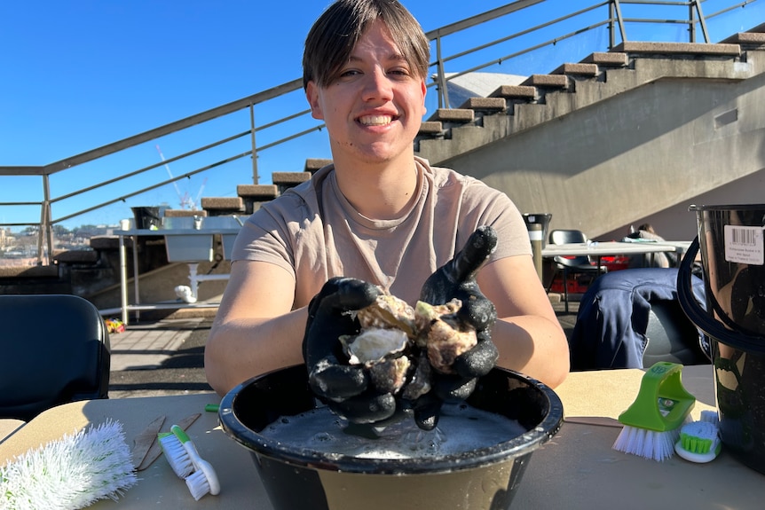 A teenage boy with black gloves and hands full of oysters. 