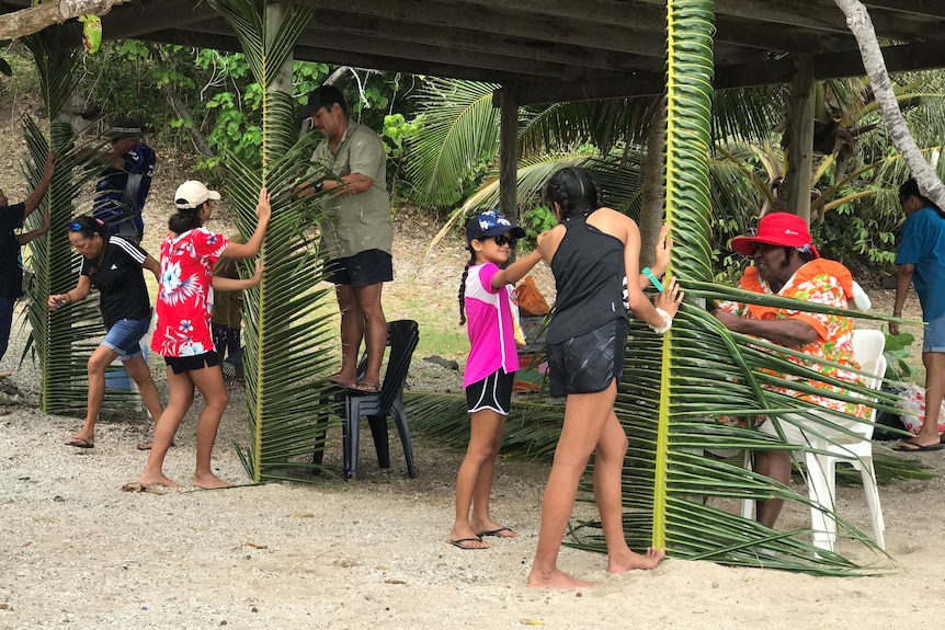 People weaving coconut leaves around shed poles.