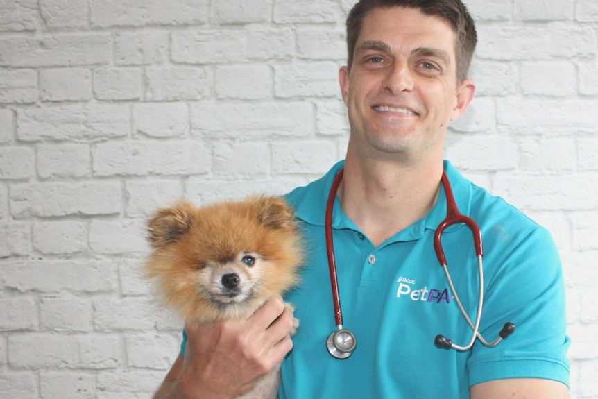 A man holding a small dog with a stethoscope around his neck 