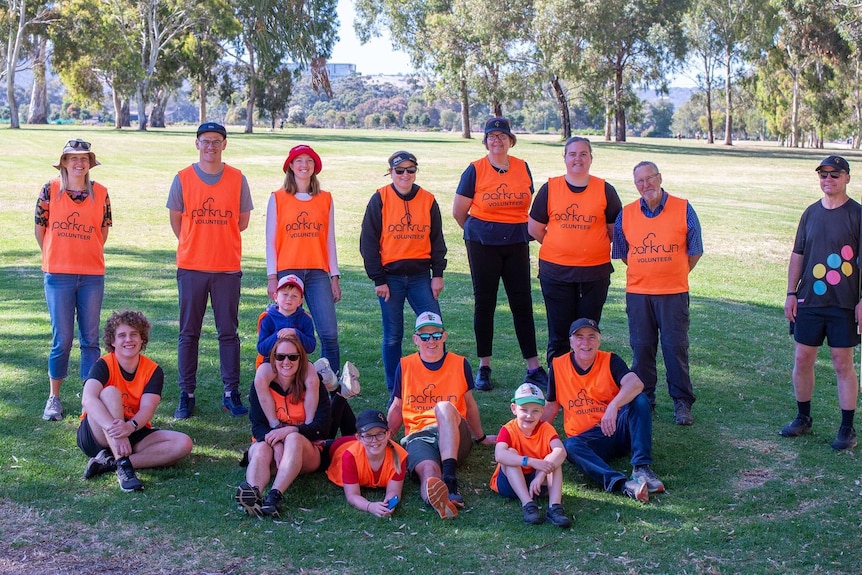 A group of people wearing orange vests gather for a photo in a park.