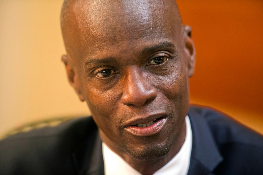 A close-up of a bald, middle-aged Haitian man in a suit looking serious.