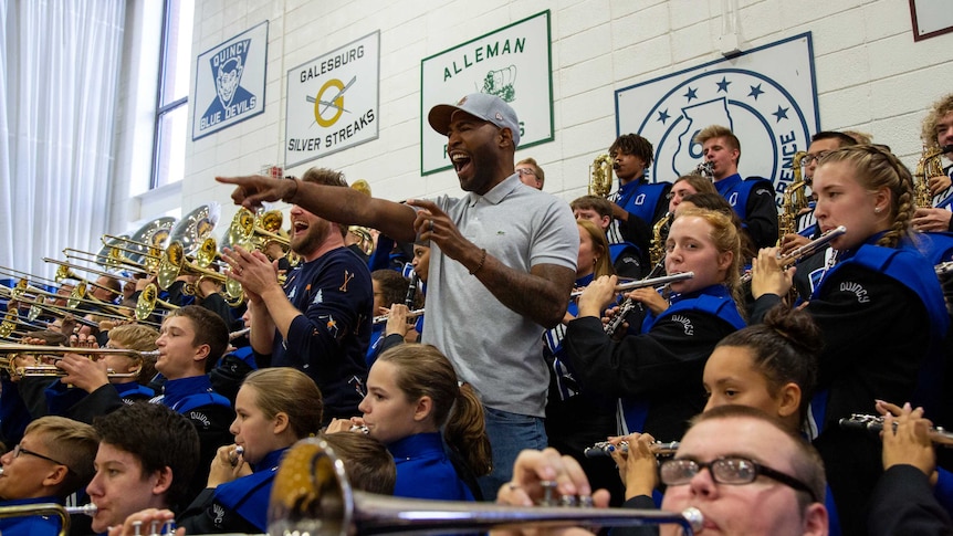 Karamo Brown points and smiles while surrounded by a high school band