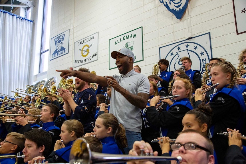 Karamo Brown points and smiles while surrounded by a high school band