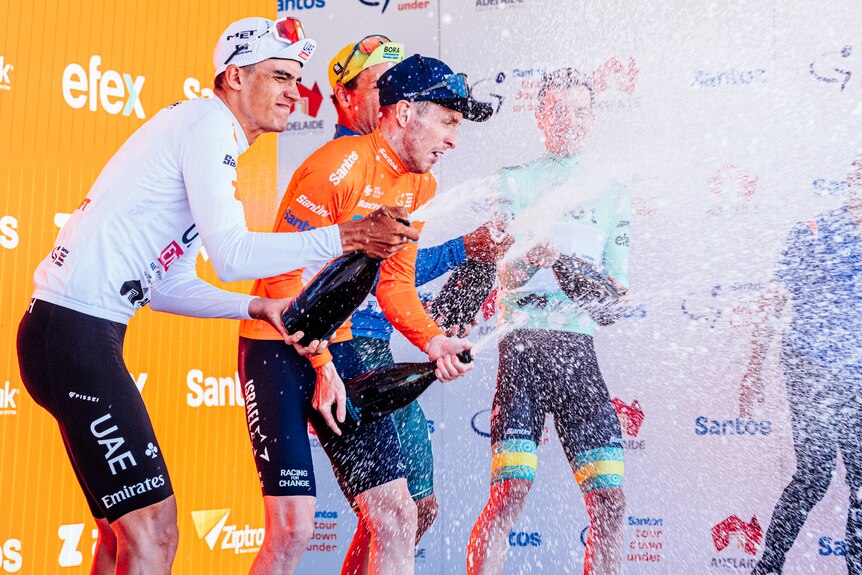 Four male cyclists spraying champagne on stage