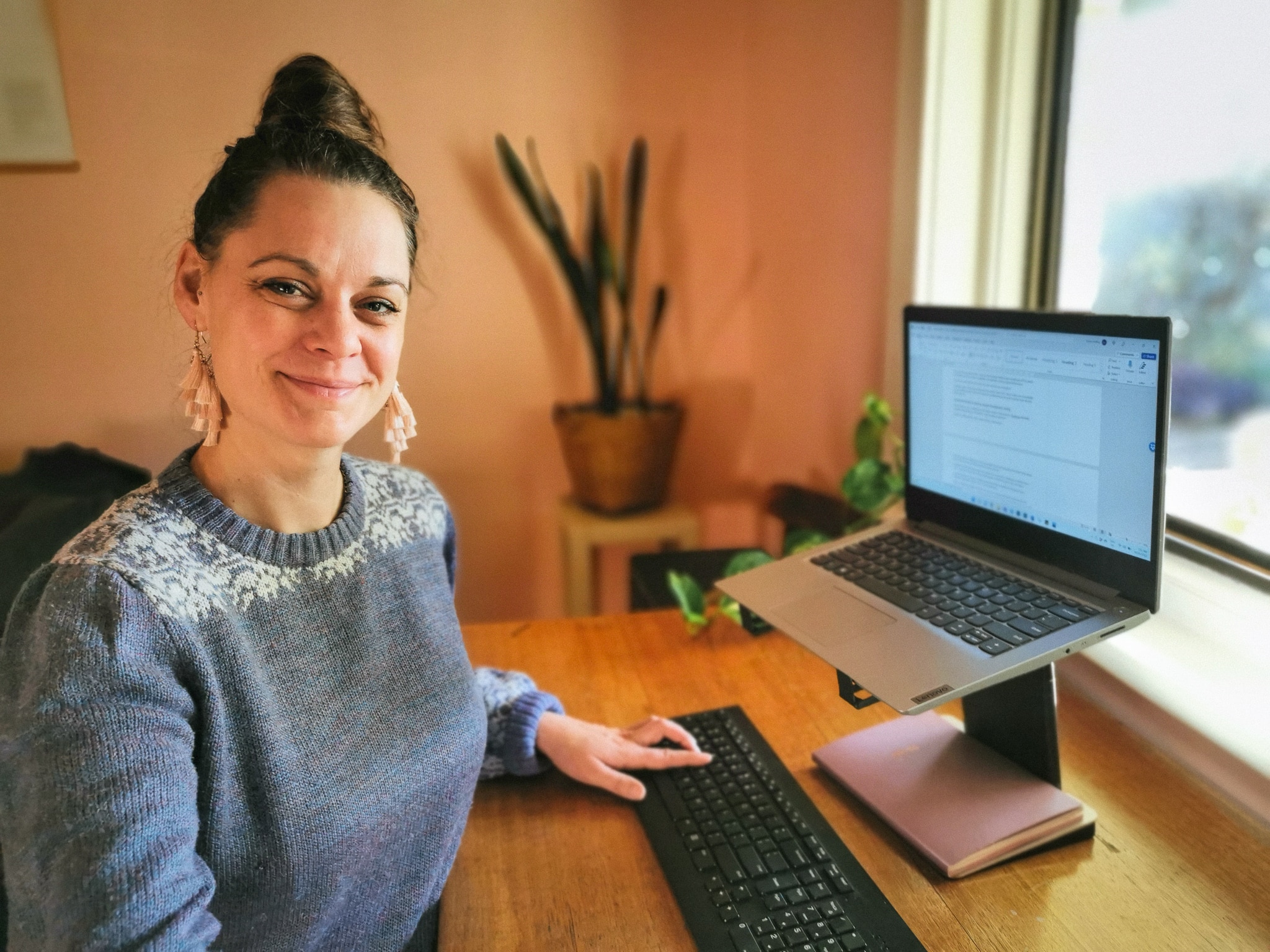 A woman stands in front of a laptop with one hand on the keyboard