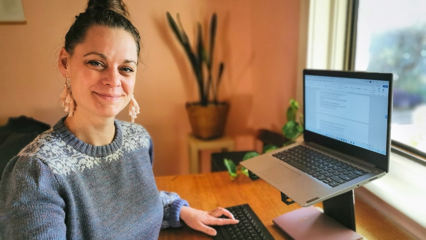 A woman stands in front of a laptop with one hand on the keyboard