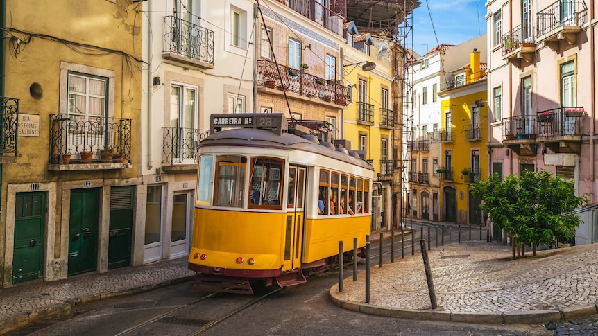 You view a bright yellow tram rising up a gentle slope on a narrow Lisbon street lined by pastel-coloured row houses.