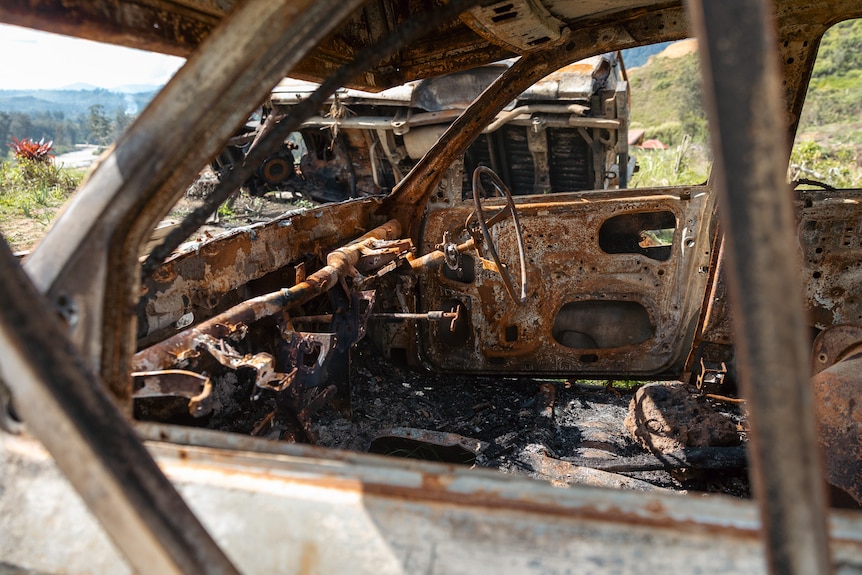 The remains of a burnt out vehicle show a charred interior, the steering wheel still visible while seats are gone