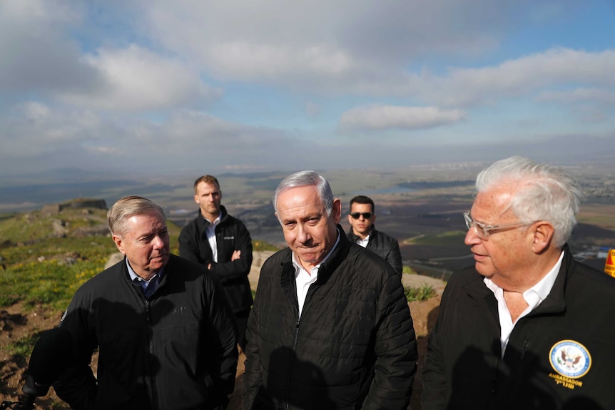 Wearing black jackets, Lindsey Graham, Benjamin Netanyahu and David Friedman stand on a mountain top.
