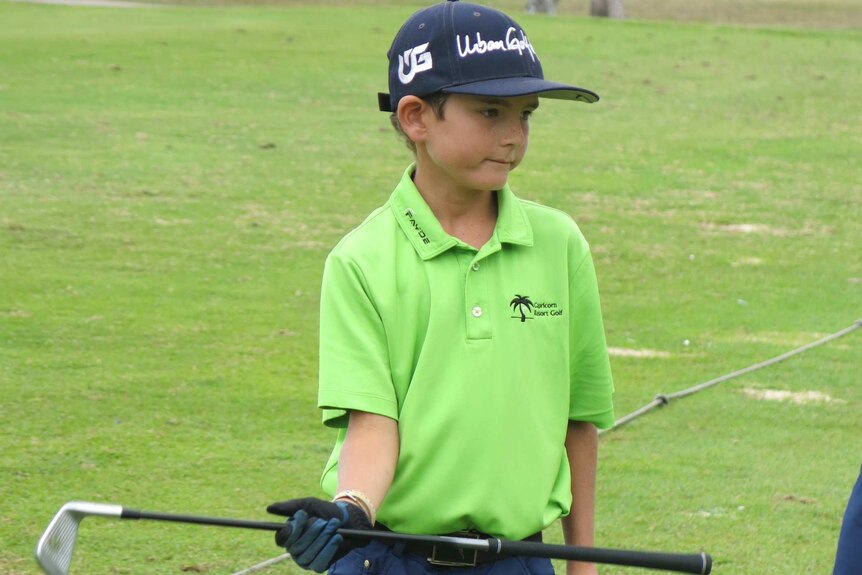 A nine-year-old boy wearing a green golf shirt at a driving range.