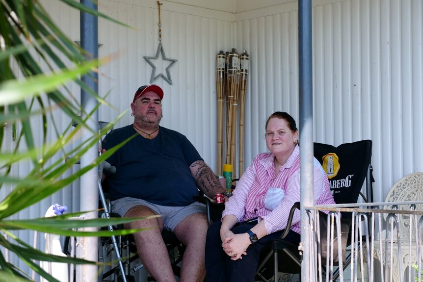 Two people sit in chairs on the front porch of a house