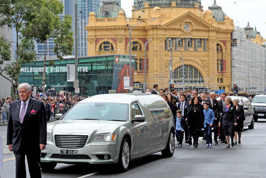 Family members walk behind the hearse of Lou Richards, in front of Flinders St station.