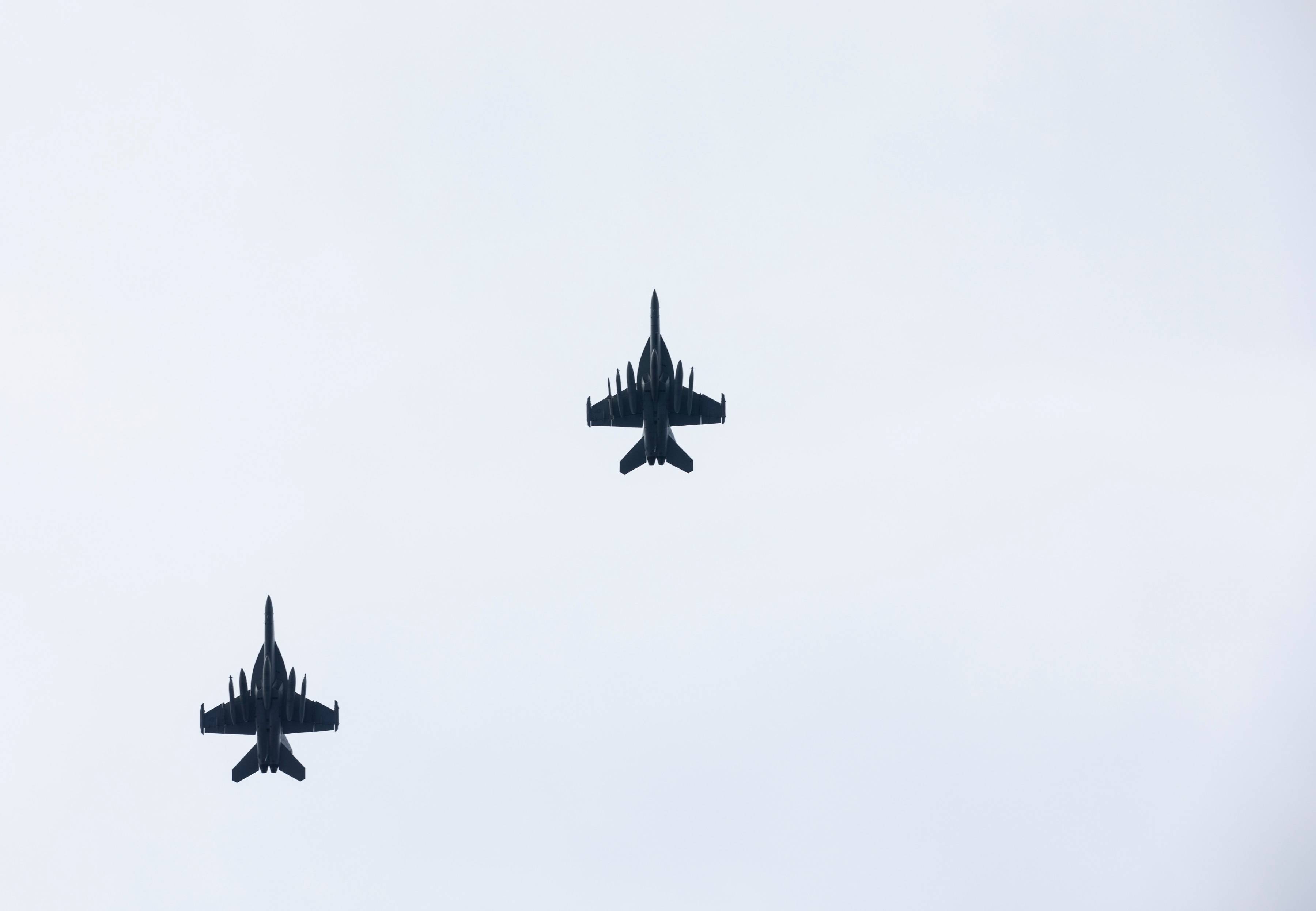 Two fighter jets fly overhead of the photographer, their silhouettes set in a blue sky.