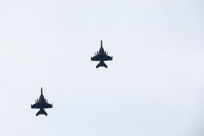 Two fighter jets fly overhead of the photographer, their silhouettes set in a blue sky.