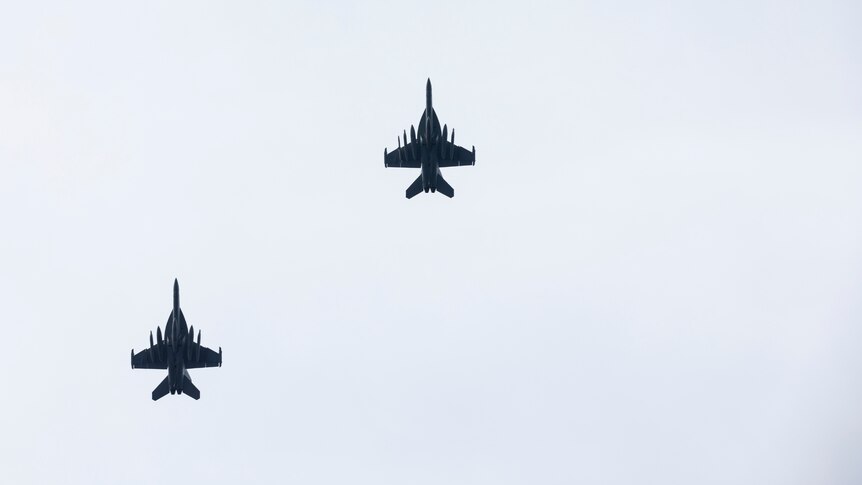 Two fighter jets fly overhead of the photographer, their silhouettes set in a blue sky.
