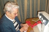 An elderly woman putting red fabric through a sewing machine
