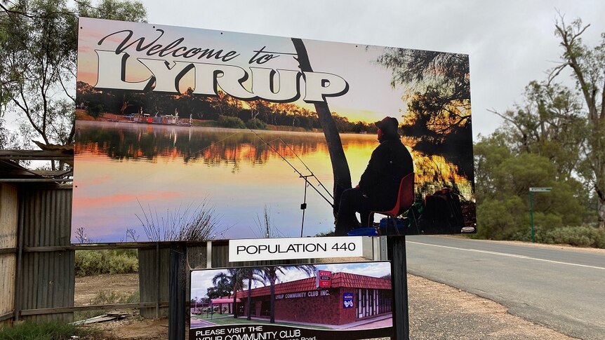 A sign on the side of a road with a picture of a man fishing. It reads "Welcome to Lyrup".