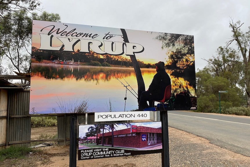 A sign on the side of a road with a picture of a man fishing. It reads "Welcome to Lyrup".