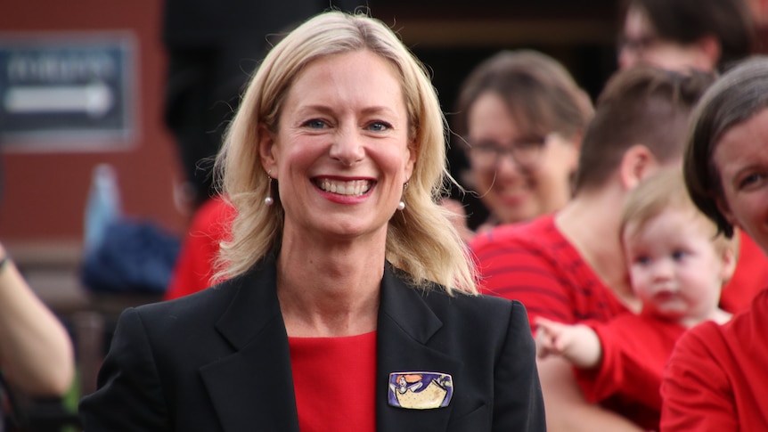 Rebecca White, wearing a red top and black jacket, smiles at the camera