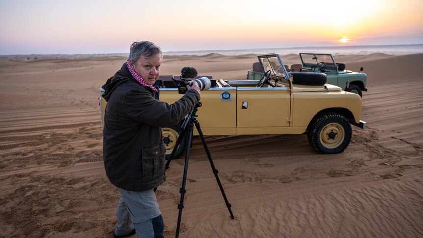 a man is in the desert pointing a camera and a microphone at two vintage looking jeeps
