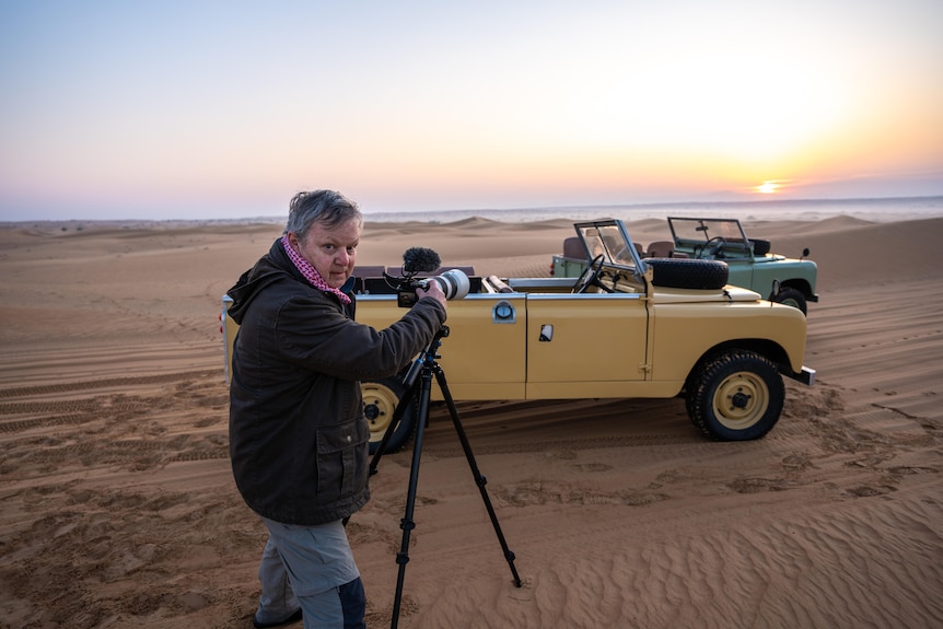 a man is in the desert pointing a camera and a microphone at two vintage looking jeeps