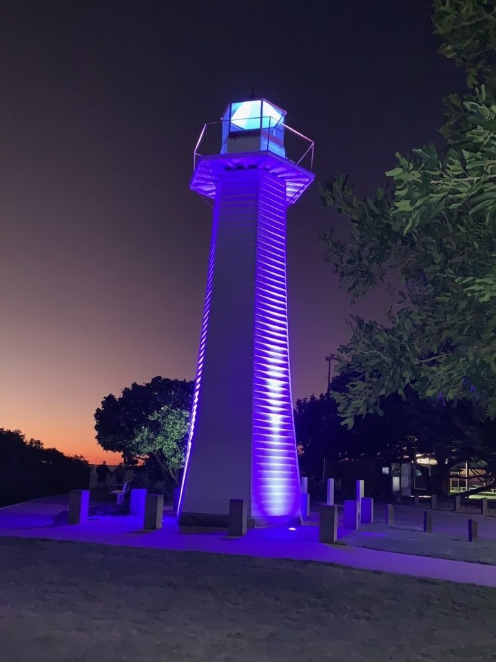 A lighthouse is illuminated by purple lighting.