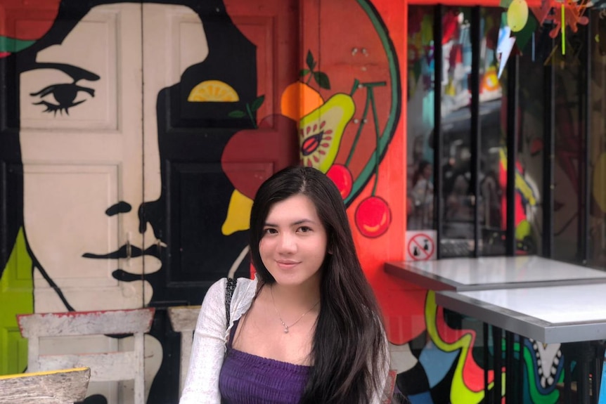 Tasya Mutiara Ramlan smiling in front of a mural.