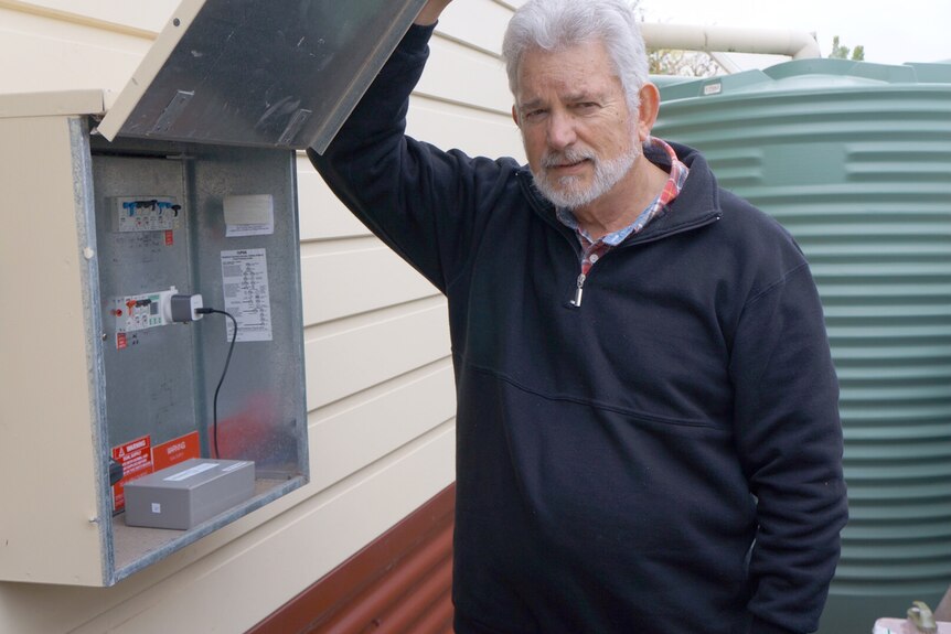 Bob Logan stands next to a power box on a wall outside the house.