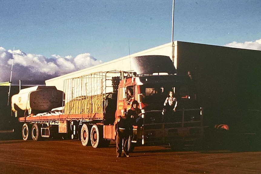 A young girl stands on a bull bar of a truck surrounded by bright red dirt in the outback and blue skies